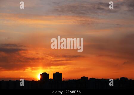 Sonnenuntergang über der Stadt, malerische Aussicht. Untergehende Sonne und orangefarbener Himmel mit dramatischen Wolken über Silhouetten von Wohngebäuden Stockfoto