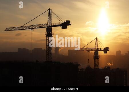 Silhouetten von Baukräne und unfertigen Wohngebäude während Schnee auf Sonnenaufgang Hintergrund. Wohnungsbau, Wohnblock Stockfoto