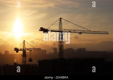 Silhouetten von Baukräne und unfertigen Wohngebäude während Schnee auf Sonnenaufgang Hintergrund. Wohnungsbau, Wohnblock Stockfoto