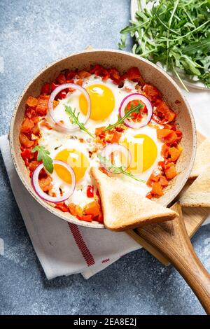 Leckere und gesunde Shakshuka in einer Bratpfanne. Eier pochiert in würziger Tomatensauce. Spiegeleier mit Toast, Rucola, lila Zwiebel Stockfoto