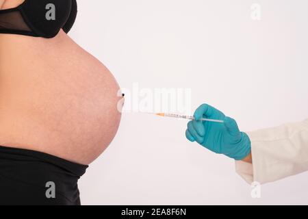 Der Bauch einer schwangeren Frau wird von einer Hand in einen Handschuh auf einem hellen Hintergrund gespritzt. Selektiver Fokus. Schwangerschaft und Impfkonzept. Stockfoto
