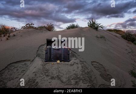 Schatzkiste am Strand bei Sonnenaufgang, Juwelen und Goldmünzen Stockfoto