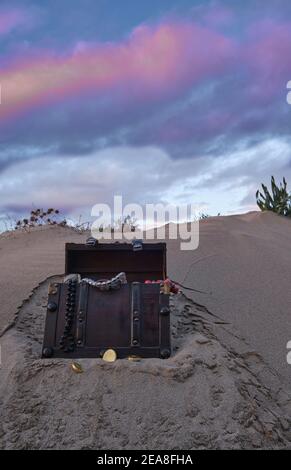 Schatzkiste am Strand bei Sonnenaufgang, Juwelen und Goldmünzen Stockfoto