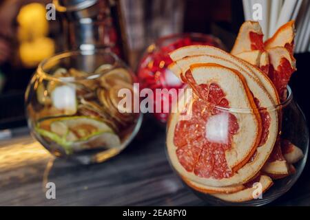 Glas mit getrockneten roten Grapefruit-Zitrusscheiben auf dem Tisch. Grauer Hintergrund mit Kopierbereich Stockfoto