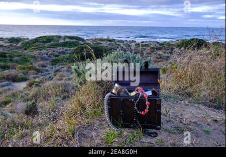 Schatzkiste am Strand bei Sonnenaufgang, Juwelen und Goldmünzen Stockfoto