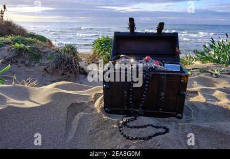 Schatzkiste am Strand bei Sonnenaufgang, Juwelen und Goldmünzen Stockfoto