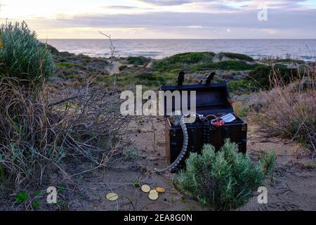 Schatzkiste am Strand bei Sonnenaufgang, Juwelen und Goldmünzen Stockfoto