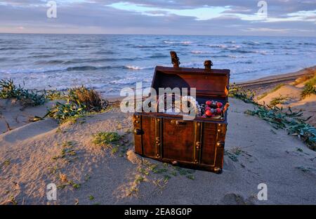 Schatzkiste am Strand bei Sonnenaufgang, Juwelen und Goldmünzen Stockfoto