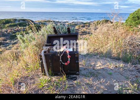 Schatzkiste am Strand bei Sonnenaufgang, Juwelen und Goldmünzen Stockfoto