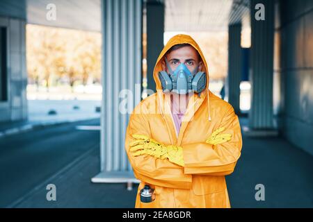 Nahaufnahme Porträt des jungen Mannes in Atemschutzmaske und Gelber Regenmantel, der auf der Straße posiert und die Kamera anschaut Stockfoto