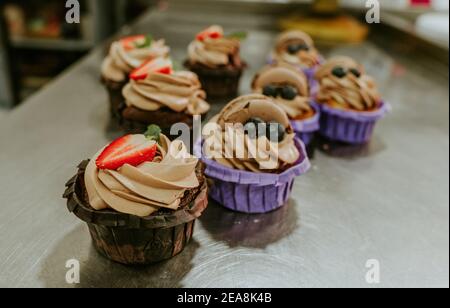 Cupcakes mit Sahne und frischen Beeren auf dem Tisch in Das Konditorei-Studio Stockfoto