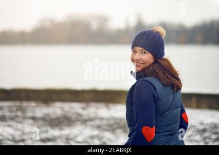 Happy mittleren Alters Brünette Frau in Pullover mit Strickmütze Drehen Und die Kamera betrachten Stockfoto