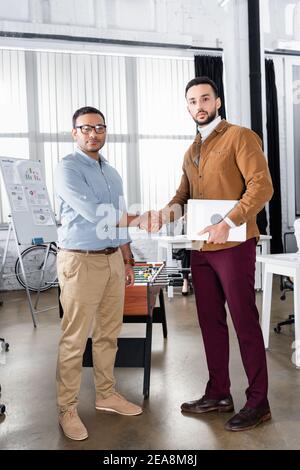 Multiethnische Geschäftsleute mit Laptop Handshake im Büro Stockfoto