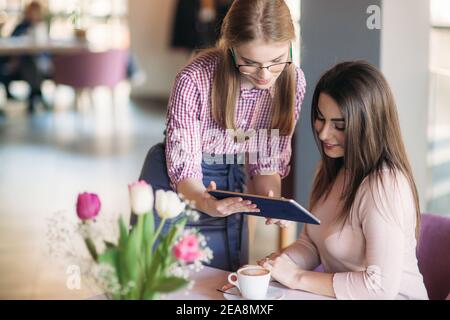 Attraktive junge Kellnerin mit einem Tablet-Computer zu nehmen Bestellen Sie bei einem Kunden in einem Café Stockfoto
