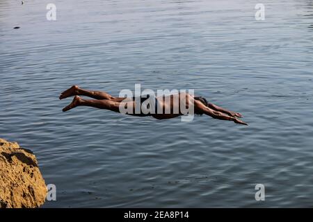 Der Mensch taucht von einer Klippe und Kopf-zuerst in den Ozean Bei Sonnenuntergang Stockfoto