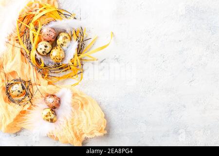 Gelbe und braune Osterquageleier mit Federn in kleinen Nestern. Geringe Schärfentiefe. Draufsicht. Leerzeichen für Text. Stockfoto