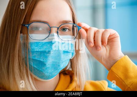 Neblige Brille trägt auf junge Frau. Nahaufnahme Porträt. Teenager Mädchen in blau medizinische Schutzmaske und Brillen Tücher verschwommen neblig beschmiert Stockfoto