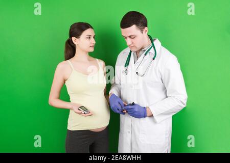 Weibliche Geburtshelferin Arzt Messung des Blutzuckers der schwangeren Frau auf buntem Hintergrund. Konzept der Gestationsdiabetes bei einem schwangeren Mädchen. Stockfoto