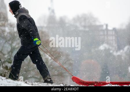 Ein Junge im Teenageralter zieht seinen Schlitten auf dem Parliament Hill im Schnee auf Hampstead Heath während des Sturms Darcy. Hampstead, London, Großbritannien 8th. Februar 2021. Wetter in Großbritannien. Stockfoto