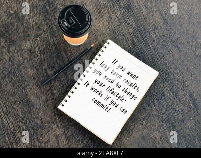 Text auf Notizblock mit Einweg-Kaffeetasse und Stift auf Holztisch Stockfoto