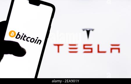 Bitcoin-Logo auf einem Smartphone gegen Tesla-Logo im Hintergrund. Stockfoto