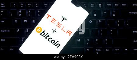 Bitcoin-Logo auf einem Smartphone gegen Tesla-Logo im Hintergrund. Stockfoto