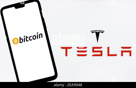 Bitcoin-Logo auf einem Smartphone gegen Tesla-Logo im Hintergrund. Stockfoto