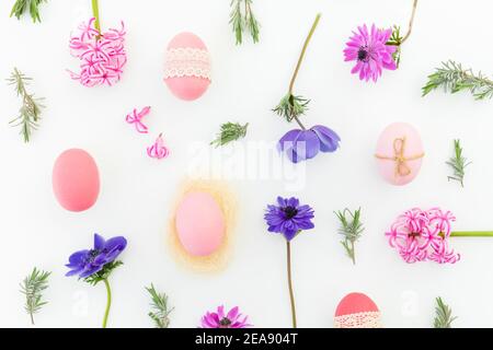 Ester Komposition mit bunten Eiern, Frühlingsblumen und Lavendelblättern auf Weiß. Flach liegend, Draufsicht Stockfoto