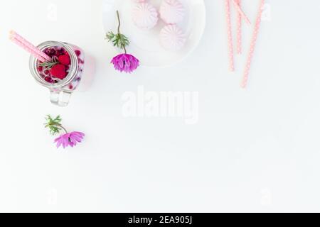 Leckerer Beerenmoothie mit Strohhalmen, Marshmallow und rosa Blüten auf weißem Hintergrund. Flach liegend. Stockfoto