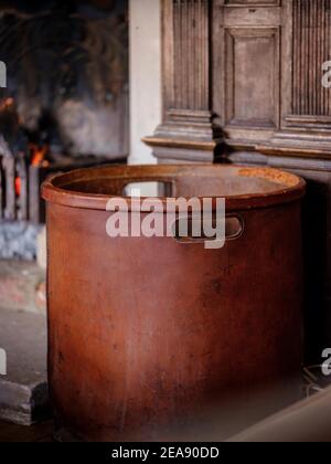 Ein ledernholzgetäfelter Korb neben einem warmen offenen Feuer mit glühender Glut in einem holzgetäfelten Landhaus. Stockfoto