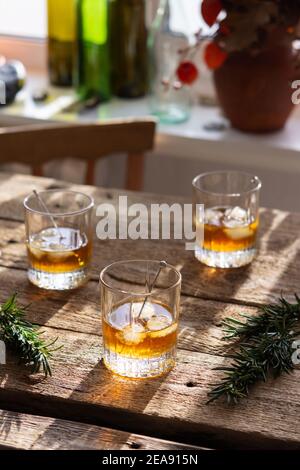 Starker Alkoholiker in Gläsern in der Sonne, Whiskey oder Gin mit Eis auf Holzgrund