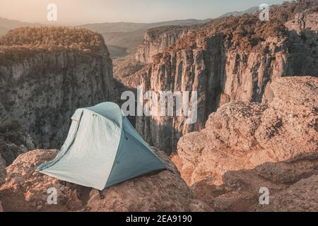 Ein eineinziges blaues Zelt befindet sich auf einer Klippe über einer tiefen Schlucht mit herrlichem Blick auf die Berge. Konzept der extremen Klettern und Camping in gefährlichen Stockfoto