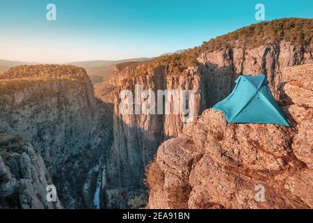 Ein eineinziges blaues Zelt befindet sich auf einer Klippe über einer tiefen Schlucht mit herrlichem Blick auf die Berge. Konzept der extremen Klettern und Camping in gefährlichen Stockfoto