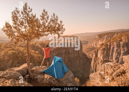 Glücklicher Wanderer mit offenen Armen auf einer Klippe mit Blick auf eine tiefe Schlucht des Tazi Canyon in der Türkei. Camping Zelt und Klettern in einer Natur Stockfoto