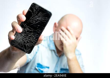 Telefon mit EINEM defekten Bildschirm Nahaufnahme. Ein weißer Mann hält ein schwarzes Smartphone mit einem geknackten Display. Stockfoto
