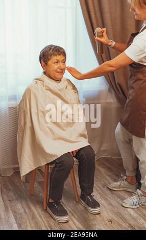 Frau schneiden ihrer älteren Mutter die Haare zu Hause. Selbstisolation Konzept Stockfoto