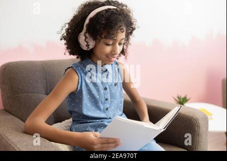Clever und wissbegierig afrikanisches präteen Schulmädchen verbringen Freizeit mit einem Buch Lesung sitzen am Sessel zu Hause, Vorbereitung auf die Prüfung Stockfoto