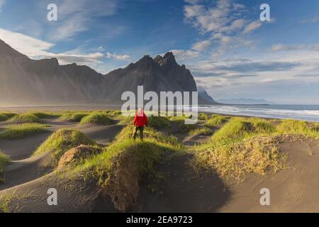 Wanderer mit Blick auf das Vestrahorn / Vesturhorn, aus Gabbro- und Granophyre-Felsen, Teil des Klifatindur-Gebirges bei Stokksnes, Island Stockfoto