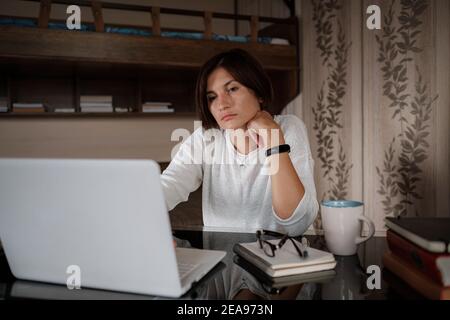 Schöne asiatische junge Frau arbeiten auf Laptop-Computer, während im Wohnzimmer sitzen. Gemütlicher Büroarbeitsplatz, Remote-Arbeit, E-Learning-Konzept Stockfoto