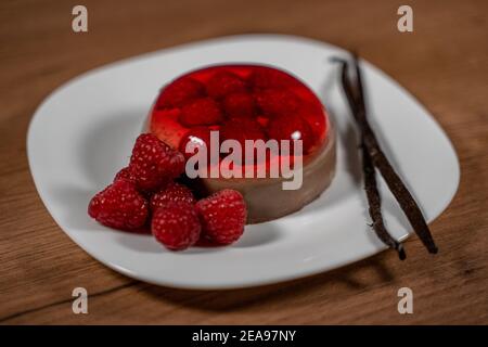 Schokopudding mit Himbeer-Gelee verziert mit frischen Himbeeren und Vanillebohnen auf weißem Teller. Nahaufnahme auf Holzoberfläche Stockfoto