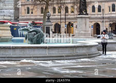 London, Großbritannien. Februar 2021, 08th. Eine Frau schaut während des Sturms Darcy auf die gefrorenen Springbrunnen auf dem Trafalgar Square in London. Kredit: SOPA Images Limited/Alamy Live Nachrichten Stockfoto