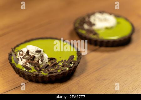 Nahaufnahme von zwei Matcha-Sahnetorten mit Schlagsahne verziert Creme und dunkle Schokolade auf Holzoberfläche Stockfoto