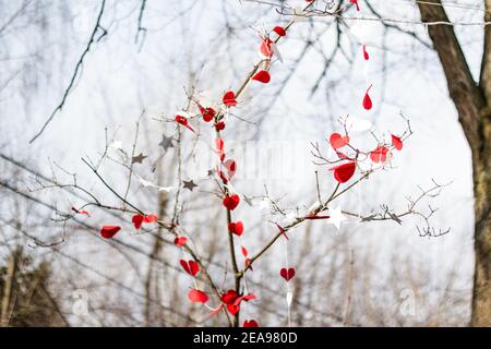 Defokussieren Sie Papierherzen. St. Valentines Dekorationen im Park. Rote und weiße handgemachte Herzen. Bäume im Park sind mit weißen und roten verziert Stockfoto