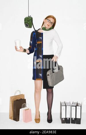 Junge Frau, rothaarig, Fotomontage, Symbolik, weißer Hintergrund, grünes Telefon, Aktenordner, Einkaufstaschen, Laptoptasche, Trinkglas aus Gläsern, Business-Outfit Stockfoto