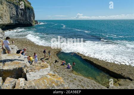 Menschen, die einen alten Steinbruch in Portland hinunter zum Dancing Ledge klettern, mit etwas Schwimmen in einem großen Felsbecken, das von den Steinbrüchen in der Nähe von Swan geschaffen wurde Stockfoto