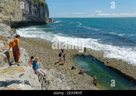 Menschen, die einen alten Steinbruch in Portland hinunter zum Dancing Ledge klettern, mit etwas Schwimmen in einem großen Felsbecken, das von den Steinbrüchen in der Nähe von Swan geschaffen wurde Stockfoto