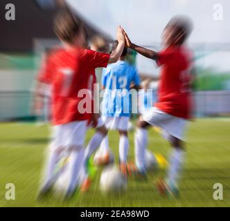 Junge Jungen in einem Team machen High Five auf Trainingseinheit. Glückliche multirassische Gruppe von Kindern Fußballspieler. Kinder machen hohe fünf als Symbol von Fai Stockfoto