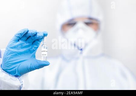 Medizinisches Personal in Hazmat Anzug, Brille und Schutzhandschuhe, hält Ampulle mit covid-19-Impfstoff Stockfoto