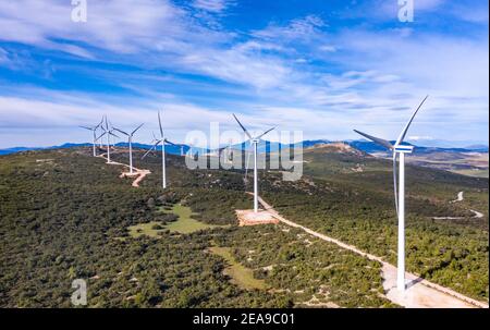 Windturbinen und kurvige Straße auf dem Hügel, Windpark Grüne ökologische Stromerzeugung. Alternative Energieanlage, blauer wolkiger Himmel, sonniger Tag, Gr Stockfoto