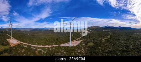 Windturbinen und kurvige Straße auf dem Hügel. Windparkpanorama, Luftdrohnenansicht. Grüne Alternative ökologische Energieerzeugung, blauer wolkig Himmel Stockfoto